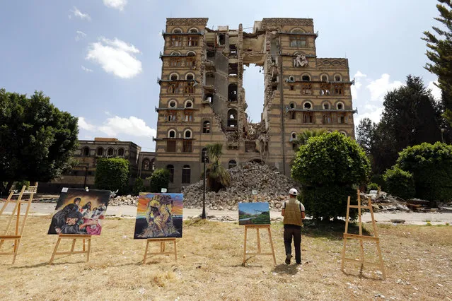 A Yemeni artist stands next to artworks during an anti-war outdoor gallery at the alleged airstrike-destroyed Republican Palace in Sana’a, Yemen, 28 March 2018. A group of Yemeni artists held the anti-war outdoor gallery using paintbrushes to illustrate the human impact of the toll conflict has taken on the Yemeni people and make the case for peace, after three years of escalating conflict in the Arab country. (Photo by Yahya Arhab/EPA/EFE)
