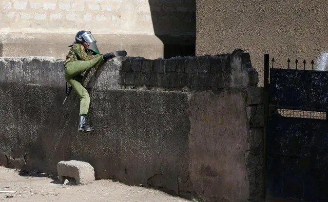 A riot police officer scales a perimeter wall as supporters of Kenya's opposition leader Raila Odinga of the Azimio La Umoja (Declaration of Unity) One Kenya Alliance, participate in a nationwide protest over cost of living and President William Ruto's government in Eastleigh neighbourhood of Nairobi, Kenya on March 20, 2023. (Photo by Thomas Mukoya/Reuters)