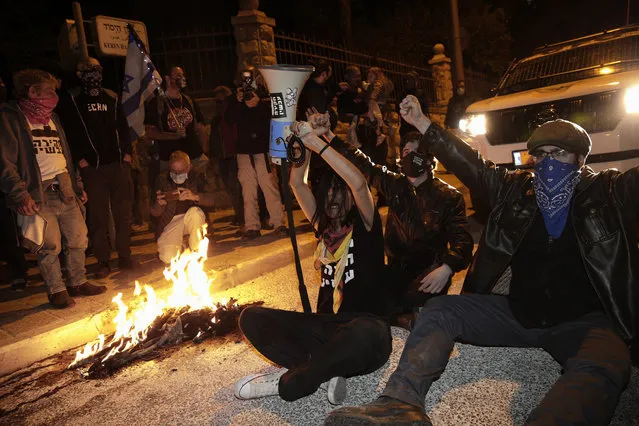 Israeli protesters chant slogans and block a road during a demonstration against Israeli Prime Minister Benjamin Netanyahu near his official residence in Jerusalem during the third nationwide coronavirus lockdown, Saturday, January 2, 2021. (Photo by Ariel Schalit/AP Photo)