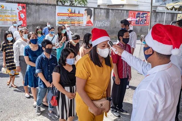 A man checks the body temperature of people entering a cathedral prior to a Christmas Eve mass, amid the coronavirus disease (CO​VID-19) pandemic, in Denpasar, Bali, Indonesia, 24 December 2020. (Photo by Made Nagi/EPA/EFE)