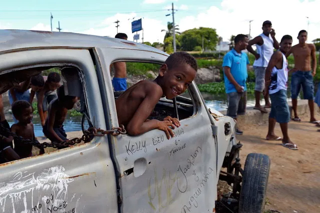 Boys look at friends playing football from an abandoned Volkswagen Beetle in a shantytown of Olinda, about 18 km from Recife in northeastern Brazil, on June 18, 2013 as the FIFA Confederations Cup Brazil 2013 football tournament is being held in the country. The historic centre of Olinda is listed as an UNESCO World Heritage Site. (Photo by Vincenzo Pinto/AFP Photo)