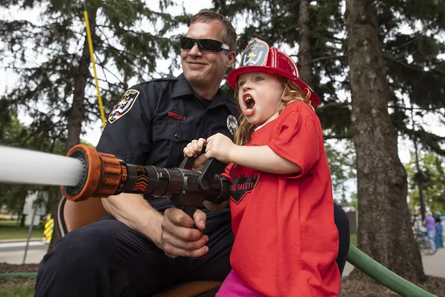 Madelyn Kettner, 5, assisted by Golden Valley firefighter Jerry Jovanovich, tries to hit a target with the high powered firefighter hose at a Public Safety Open House at Golden Valley Fire Station 1, Wednesday, June 20, 2018, in Golden Valley, Minn. Activities included a live burn demonstration, squirt house, fire truck tours, police squad car tours, K-9 demonstrations, a pizza party raffle and more. (Photo by Leila Navidi/Star Tribune via AP Photo)