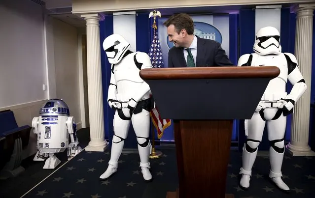 White House press secretary Josh Earnest and Star Wars Stormtroopers wait for Star Wars Robot R2-D2 (L) to enter the briefing room after U.S. President Barack Obama finished his end of the year news conference at the White House in Washington December 18, 2015.  The Star Wars characters were at the White House for a private screening of Star Wars: The Force Awakens' which was shown to first lady Michelle Obama and Gold Star Families. (Photo by Kevin Lamarque/Reuters)