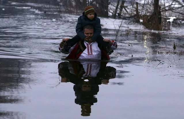 A man carries a child on his shoulders as he dances in the icy waters of the Tundzha river during a celebration for Epiphany Day in the town of Kalofer, Bulgaria January 6, 2016. (Photo by Stoyan Nenov/Reuters)