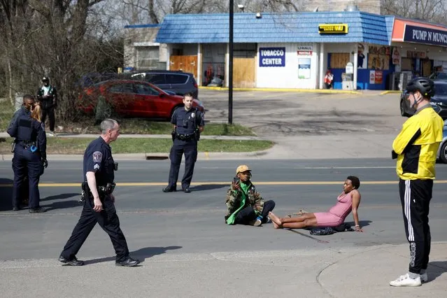 Phoenix Robles and Dorcas Monari sit on the ground as they block road traffic on Humboldt Avenue in front of the Brooklyn Center Police Department as protests continue days after former police officer Kim Potter fatally shot Daunte Wright, in Brooklyn Center, Minnesota, U.S., April 18, 2021. (Photo by Nick Pfosi/Reuters)