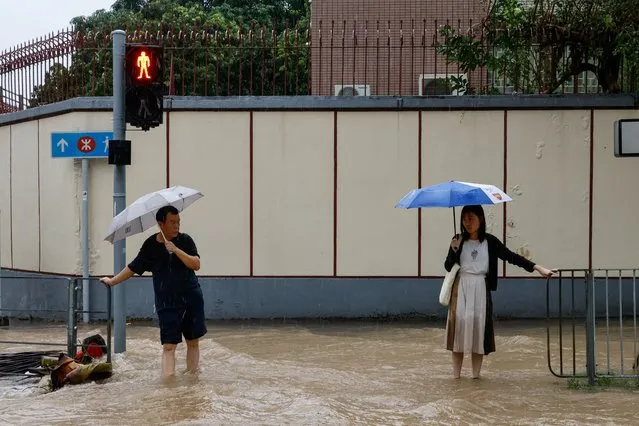 People hold railing to keep their position in a flooded area after heavy rains, in Hong Kong, China on September 8, 2023. (Photo by Tyrone Siu/Reuters)