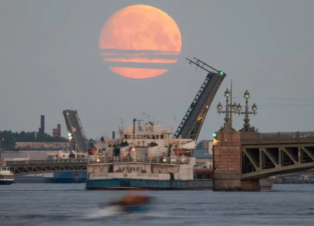 A cargo ship travels past as drawbridges rise above the Neva River, with the moon in the sky, in St. Petersburg, Russia, early Tuesday, May 25, 2021. (Photo by Dmitri Lovetsky/AP Photo)