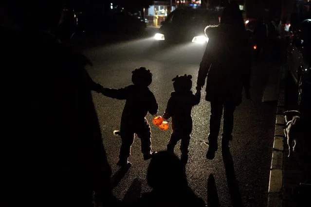 Two children dressed in their Halloween costumes hold pumpkin-shaped lanterns while walking on their way to ask for candies from neighbors the night before Halloween in Beijing, China, Wednesday, October 30, 2013. (Photo by Alexander F. Yuan/AP Photo)