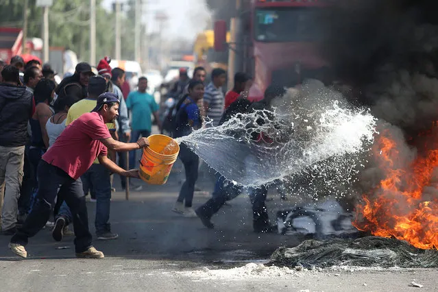 A man throws water on burning tires during a protest against the rising prices of gasoline enforced by the Mexican government at the side of a Pemex gas station in San Miguel Totolcingo , Mexico, January 3, 2017. (Photo by Edgard Garrido/Reuters)