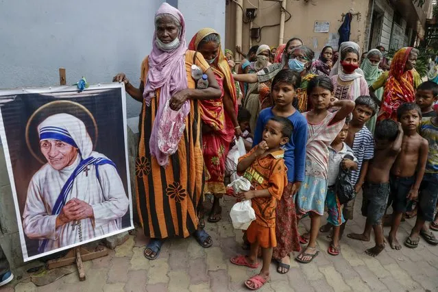 Homeless people gather beside a portrait of Saint Teresa, the founder of the Missionaries of Charity, to collect free food outside the order's headquarters in Kolkata, India, Thursday, August 26, 2021. Thursday marked the birth anniversary of Nobel laureate Mother Teresa, a Catholic nun who spent 45-years serving the poor, the sick, the orphaned, and the dying. (Photo by Bikas Das/AP Photo)