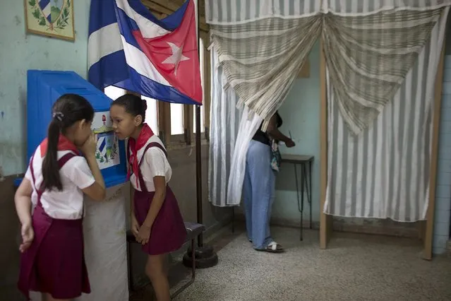 Ten-year-old schoolgirls Claudia Fuentes (R) and Laura Gonzales chat as an elector casts her vote at a poling station in Havana, April 19, 2015. (Photo by Alexandre Meneghini/Reuters)
