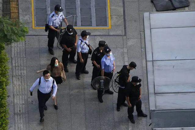 Residents past by police and security personnel preparing for duty outside the Evergrande headquarters in Shenzhen, China, Friday, September 24, 2021. Things appeared quiet at the headquarters of the heavily indebted Chinese real estate developer Evergrande, one day after the day it had promised to pay interest due to bondholders in China. (Photo by Ng Han Guan/AP Photo)