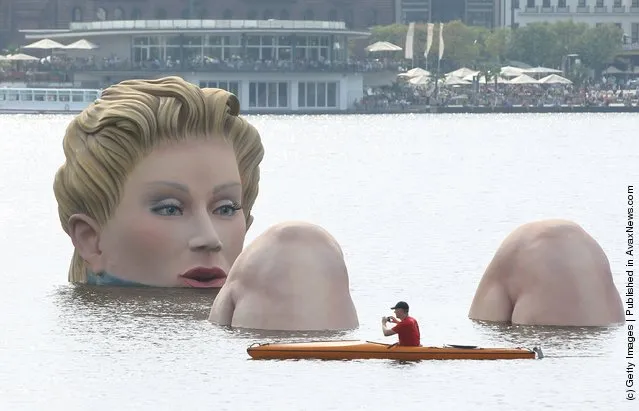 People in boats approach Die Badende (The Bather), a giant sculpture showing a woman's head and knees as if she were resting in the Binnenalster lake in Hamburg, Germany