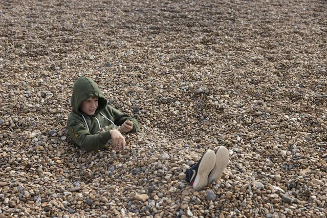A boy buries himself in the shingle on September 26, 2021 in Brighton, England. Brighton is playing host to the Labour party's 2021 conference from Saturday 25 to Wednesday 29 September (Photo by Dan Kitwood/Getty Images)