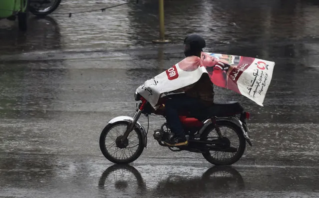 A Pakistani man wears a poster to protect himself from the rain as he rides his motorbike on a road in Lahore on January 31, 2019. (Photo by Arif Ali/AFP Photo)