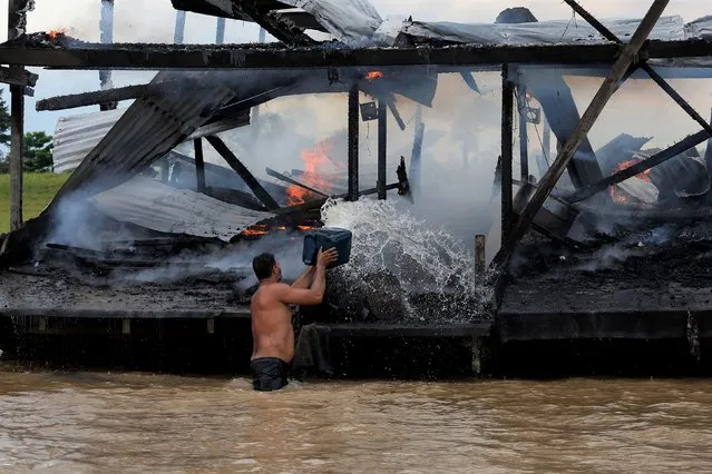 An illegal miner throws water at one of the more than 60 dredging barges that were set on fire by officers of the Brazilian Institute of the Environment and Renewable Natural Resources, IBAMA, during an operation to try to contain illegal gold mining on the Madeira river, a tributary of the Amazon river in Borba, Amazonas state, Brazil, Sunday, November 28, 2021. Hundreds of barges belonging to illegal miners had converged on the river during a gold rush in the Brazilian Amazon prompting IBAMA authorities to start burning them. (Photo by Edmar Barros/AP Photo)