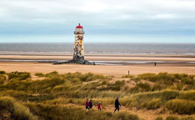 People walk past the Point of Ayr lighthouse, a grade II-listed building on the north coast Talacre, Wales, UK on February 20, 2017. (Photo by Peter Byrne/PA Wire)