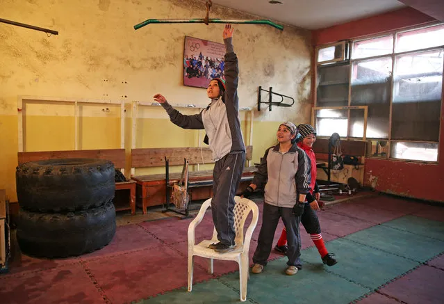 In this Wednesday, March, 5, 2014 photo, an Afghan female boxer, left, tries to do pull-ups during a practice session at the Kabul Stadium boxing club, Afghanistan. The Afghanistan National Olympic Committee boxing club has fewer than a dozen women and little money for them. Previously nongovernmental organizations supported them. At that time there were 25 young women who received a salary the equivalent of $100 per month and transportation to and from the Kabul Stadium where they train. (Photo by Massoud Hossaini/AP Photo)