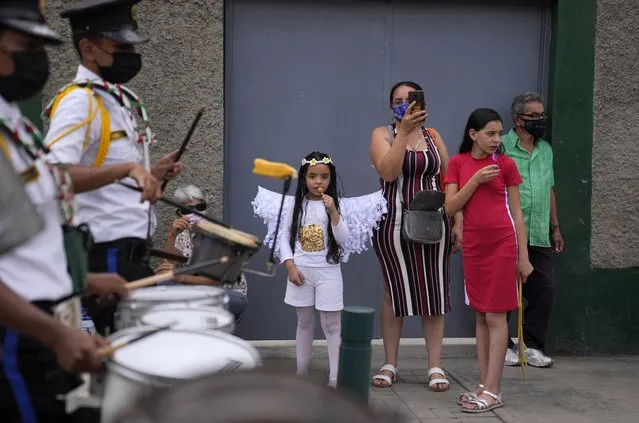 Residents look at school marching band during a parade by mothers and children form a soup kitchen celebrating Christmas in the Antimano neighborhood of Caracas, Venezuela, Thursday, December 16, 2021. (Photo by Ariana Cubillos/AP Photo)