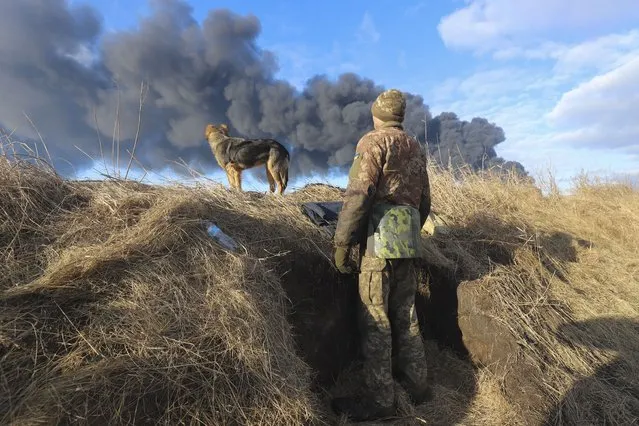 A Ukrainian serviceman and his dog stands in a position looking at smoke from a burned petroleum storage depot behind after a Russian missile attacked near Kiev, Ukraine, 27 February 2022. Russian troops entered Ukraine on 24 February prompting the country's president to declare martial law and triggering a series of announcements by Western countries to impose severe economic sanctions on Russia. (Photo by Alisa Yakubovych/EPA/EFE)