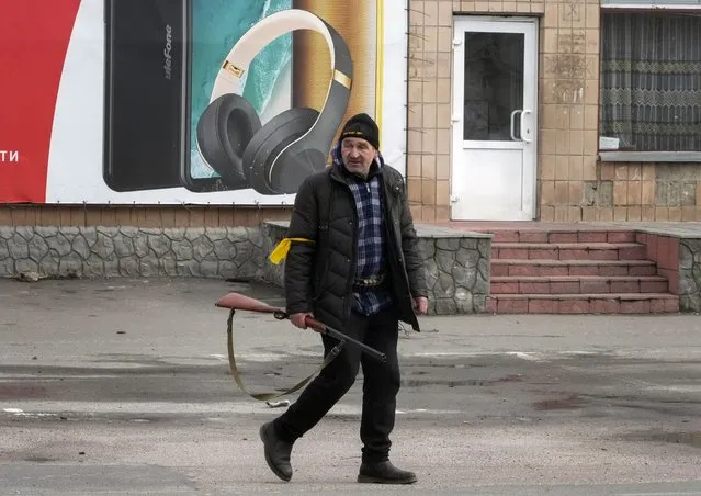 A local resident holding a hunting rifle walks in the central square of the town of Makariv, 60 kilometers west of Kyiv, Ukraine, Friday, March 4, 2022. Russia's war on Ukraine is now in its ninth day and Russian forces have shelled Europe's largest nuclear power plant, sparking a fire there that was extinguished overnight. (Photo by Efrem Lukatsky/AP Photo)