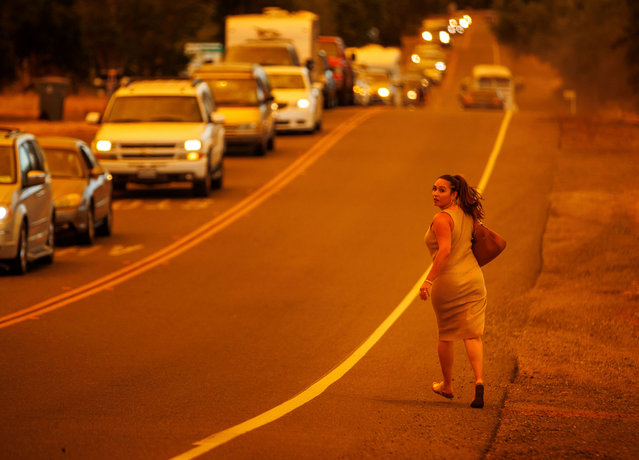 A women runs while cars evacuate as the Thompson Fire burns, Tuesday, July 2, 2024, in Oroville, Calif. (Photo by Ethan Swope/AP Photo)