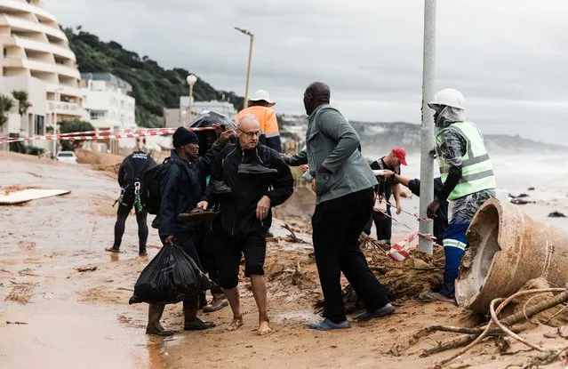 Local residents move to safety aftet they were trapped following heavy rains and winds in Umdloti north of Durban, on May 22, 2022. Floods, mudslides and rainstorms struck the South African port city of Durban and surrounding KwaZulu-Natal province. (Photo by Rajesh Jantilal /AFP Photo)