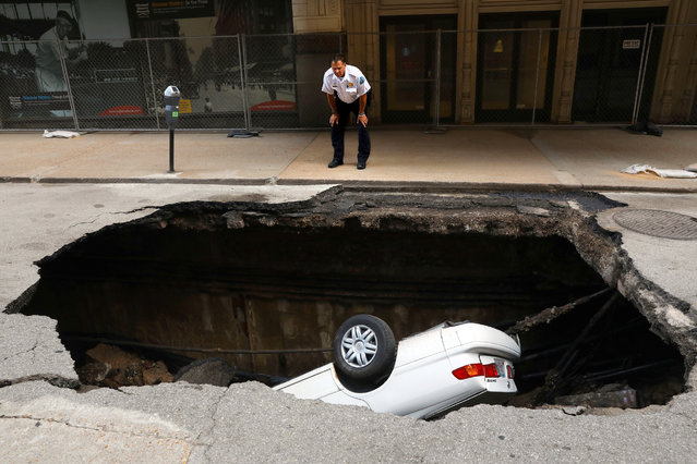 A St. Louis police officer looks over a large hole in 6th Street, Thursday, June 29, 2017, in St. Louis, that swallowed a Toyota Camry between Olive and Locust Streets. It isn't immediately clear what caused the collapse. (Photo by Christian Gooden/St. Louis Post-Dispatch via AP Photo)