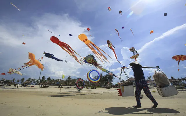 In this Sunday, June 11, 2017, photo, a food vender walks under flying kites on Tam Thanh beach during an International Kite Festival in Quang Nam province, Vietnam. Hundreds of flying giant sea creatures, animal shaped and folklore inspired kites from 20 countries were taken to the sky. (Photo by Hau Dinh/AP Photo)