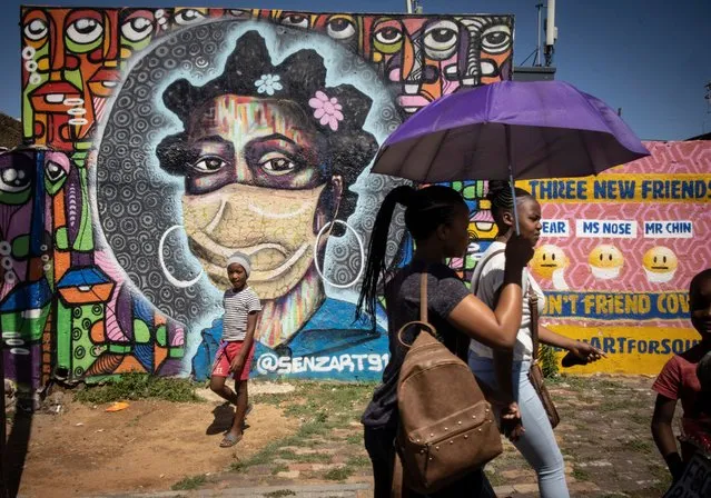 Soweto residents walk in front of an informative graffiti art work educating local Soweto residents about the dangers of the coronavirus, Johannesburg, South Africa, 30 November 2021. South Africa's government is considering mandatory vaccinations for all citizens as it tries to educate and vaccinated its population after the new Omicron variant of SARS-CoV-2, the virus that causes COVID-19, was detected. Several countries banned travel with Southern African countries including South Africa due to the Omicron variant. (Photo by Kim Ludbrook/EPA/EFE)