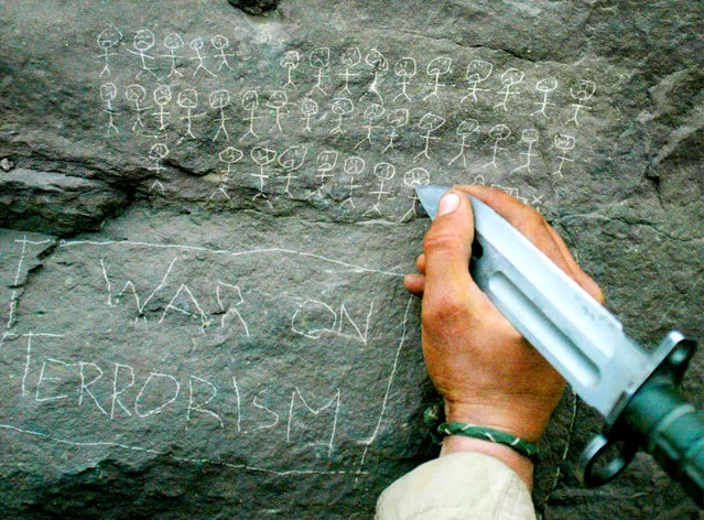 United States Army 10th Mountain Division soldier Jorge Avino from Miami, Florida carves the body count that their mortar team has chalked up on a rock, March 9, 2002 near the villages of Sherkhankheyl, Marzak and Bobelkiel, in Afghanistan. (Photo by Joe Raedle/Reuters)