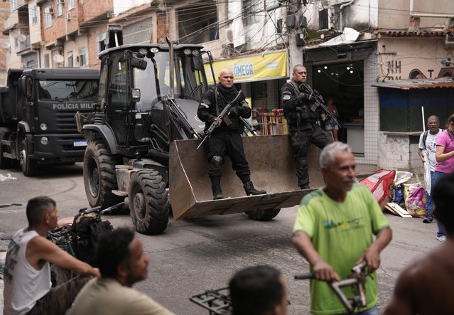 Police ride past residents in a bulldozer they use to clear street barricades during a security operation against organized crime in the Mare Complex favela of Rio de Janeiro, Brazil, Monday, October 9, 2023. Security forces targeted three neighborhoods that are controlled by the Red Command drug trafficking group. (Photo by Silvia Izquierdo/AP Photo)