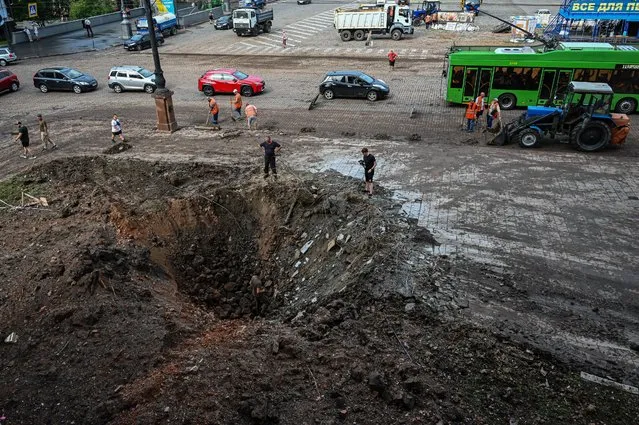 Municipal service workers stand near a crater near the damaged headquarters of the Kharkiv administration building following an overnight missile strike in Kharkiv, on August 29, 2022, amid Russia's military invasion launched on Ukraine. (Photo by Sergey Bobok/AFP Photo)