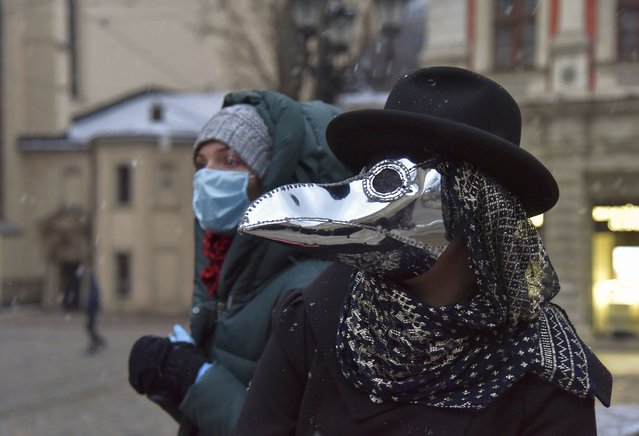 A woman wearing a protective mask is seen behind a girl dressed in a Plague Doctor Mask in Western-Ukrainian city of Lviv, Ukraine, 22 March 2020. Ukrainian Designer Anastasia Markovska sewed protective masks looking like Plague Doctor Masks, the traditional costume of Venice Carnival, for herself and her friends due to the ongoing pandemic of the COVID-19 disease caused by the SARS-CoV-2 coronavirus. In Ukraine had been 47 laboratory-confirmed cases of COVID-19, including three deaths and one recovery as Ukraine's Health Ministry announced. (Photo by Pavlo Palamarchuk/EPA/EFE)
