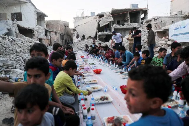 Children eat their Iftar meal provided by a group of volunteers in a damaged neighbourhood, amid fear for the coronavirus disease (COVID-19) outbreak, in Atarib, Aleppo countryside, Syria, May 7, 2020. (Photo by Khalil Ashawi/Reuters)