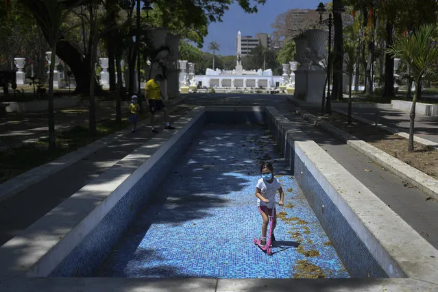 A child wearing a face mask rides her scooter inside an empty water fountain at Los Proceres boulevard in Caracas, Venezuela, Sunday, April 26, 2020. Venezuela’s government allowed for children to go outside and play for eight hours, after it had imposed quarantine to help stop the spread of the new coronavirus. (Photo by Matias Delacroix/AP Photo)