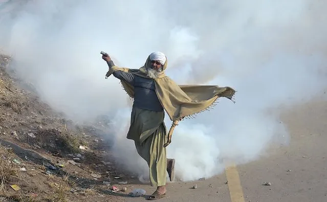 A Pakistani protester of the Tehreek-i-Labaik Yah Rasool Allah Pakistan (TLYRAP) religious group throws a tear gas shell back towards police during a clash in Islamabad on November 25, 2017. Pakistani forces fired rubber bullets and lobbed tear gas at protesters in Islamabad on November 25 as they moved to disperse an Islamist sit-in that has virtually paralysed the country's capital for weeks. The roughly 8,500 elite police and paramilitary troops in riot gear began clearing the 2,000 or so demonstrators soon after dawn, with nearby roads and markets closed. (Photo by Aamir Qureshi/AFP Photo)