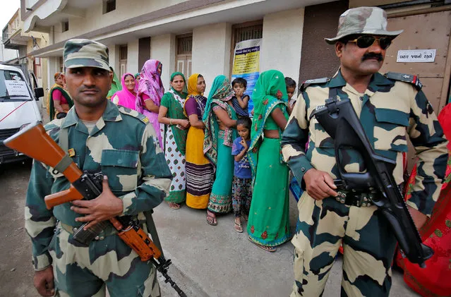 Border Security Force (BSF) soldiers stand guard as women wait in a queue to cast their votes at a polling booth during the first phase of state assembly election in Surendranagar district in Gujarat, India, December 9, 2017. (Photo by Amit Dave/Reuters)