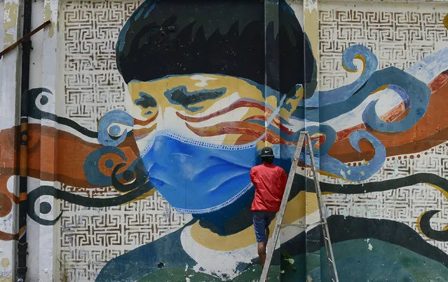 A street artist spray paints a protective face mask over an old mural featuring a Venezuelan Indigenous man, in Caracas, Venezuela, Saturday, July 18, 2020, amid the new coronavirus pandemic. (Photo by Matias Delacroix/AP Photo)