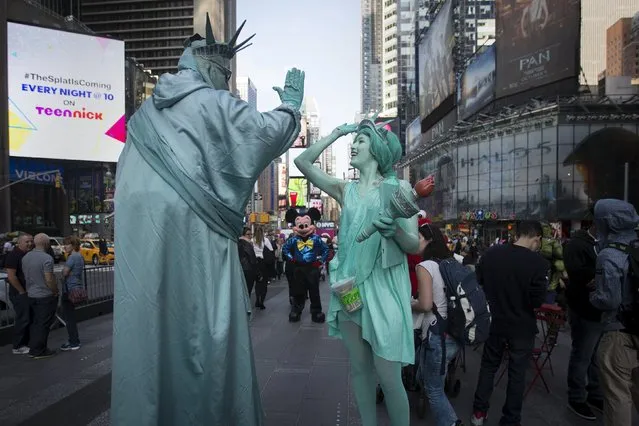 A woman (R) who gave her name as Allyson, and who is dressed up as the Statue of Liberty high fives as she teases and harasses a man who is also dressed up as a Statue of Liberty while she films a comedy segment in Times Square in the Manhattan borough of New York October 8, 2015. The woman was following the man who poses for tips with tourists around and joking with him. (Photo by Carlo Allegri/Reuters)