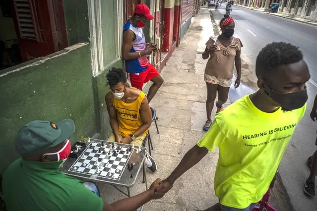 People wearing masks as a precaution against the spread of the new coronavirus walk on a street while others play chess on a sidewalk in Havana, Cuba, Wednesday, September 23, 2020. The Trump administration tightened sanctions against Cuba Wednesday, prohibiting travelers from bringing rum and cigars into the U.S. and issuing an expanded list of hotels and tourist venues that Americans can no longer book for stays on the island. (Photo by Ramon Espinosa/AP Photo)