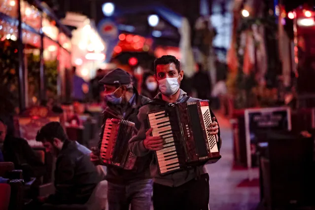 Entertainers playing accordions, wearing face masks for protection against the COVID-19 infection walk by restaurants in the old part of Bucharest, Romania, Friday, October 23, 2020. Romania's daily tally of coronavirus infections rose above 5,000 for the first time and patients in intensive care units also reached a new high as health officials reported 5,028 cases and 82 deaths in the last 24 hours and intensive care units across the country were treating 782 people for the coronavirus. (Photo by Vadim Ghirda/AP Photo)