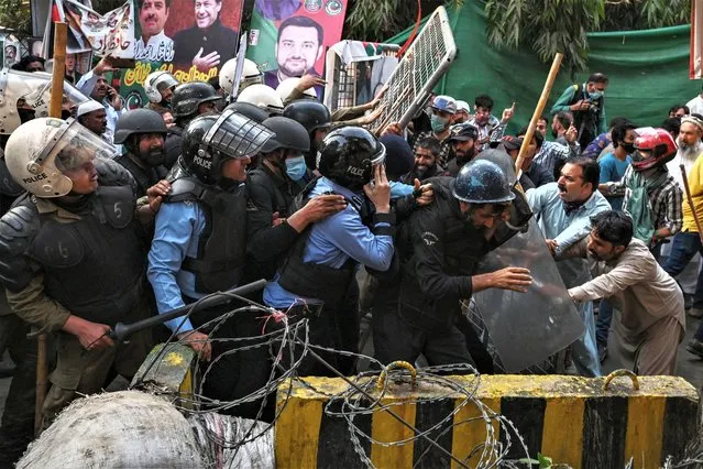 Supporters (R) of former prime minister Imran Khan try to stop riot police scuffle outside Khan's house to prevent officers from arresting him, in Lahore on March 14, 2023. (Photo by Arif Ali/AFP Photo)