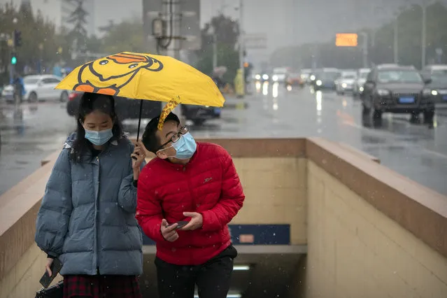 People wearing face masks to protect against the coronavirus hold an umbrella as they walk through the first snowfall of the season in Beijing, Saturday, Nov. 21, 2020. China is starting mass testing on 3 million people in a section of the northern city of Tianjin and has tested thousands of others in a hospital in Shanghai after the discovery of a pair of cases there. (Photo by Mark Schiefelbein/AP Photo)
