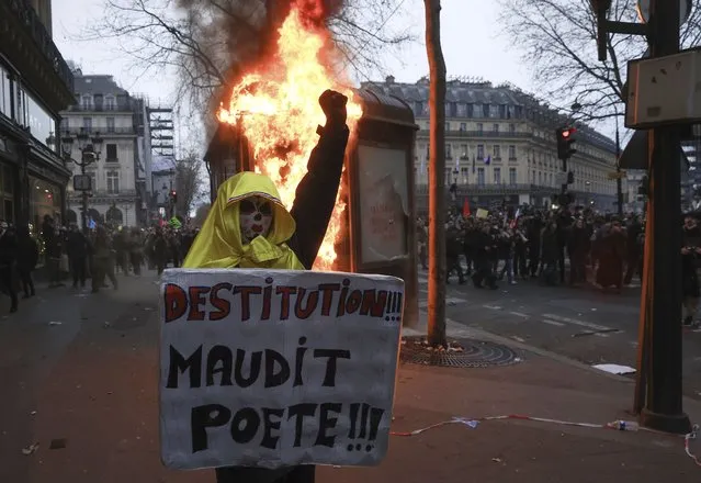 A protester holds a placard that reads, “destitution of the cursed poet” during a rally in Paris, Thursday, March 23, 2023. French unions are holding their first mass demonstrations Thursday since President Emmanuel Macron enflamed public anger by forcing a higher retirement age through parliament without a vote. (Photo by Aurelien Morissard/AP Photo)