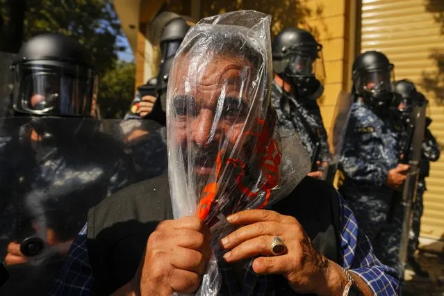 A retired member of Lebanese security forces uses a plastic bag to protect him self from tear gas during clashing with the Lebanese army and riot police during a protest in Beirut, Lebanon, Tuesday, April 18, 2023. (Photo by Hussein Malla/AP Photo)
