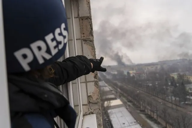 Associated Press photographer Evgeniy Maloletka points at the smoke rising after an airstrike on a maternity hospital, in Mariupol, Ukraine, Wednesday, March 9, 2022. (Photo by Mstyslav Chernov/AP Photo)