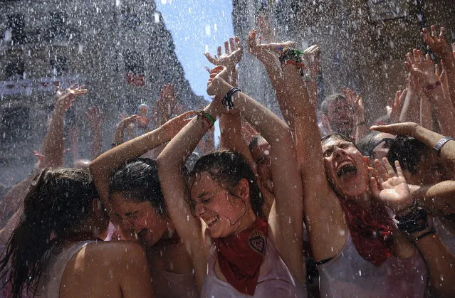 Revelers enjoy being sprayed with water from a balcony in Ayuntamiento square, in Pamplona, northern Spain on Saturday, July 6, 2013, as they celebrate the start of Spain's most famous bull-running festival with the annual launch of the “chupinazo” rocket. (Photo by Alvaro Barrientos/AP Photo)