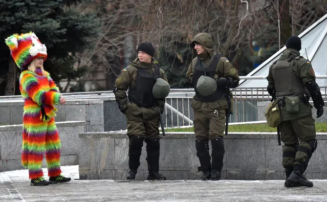 Ukrainian National Guard members walk past a woman wearing a colourful costume as they patrol near Independence Square in Kiev on November 22, 2016 following a night of violence by activists of some far-right Ukrainian parties. Kiev police said they were investigating an attack by far-right activists on a Russian bank and the office of a Ukrainian politician who is close friends with Kremlin chief Vladimir Putin. Ukraine had marked the third anniversary of the start of three months of protests that resulted in the country's Russian-backed former president being ousted in February 2014 as the former Soviet republic set on a pro-European Union course. (Photo by Sergei Supinsky/AFP Photo)