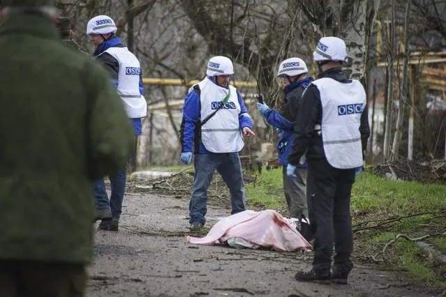 OSCE members prepare to carry a body of Ukrainian soldier killed on Saturday, April 18, near the village of Shyrokyne, eastern Ukraine, Sunday, April 19, 2015. Though fighting has diminished substantially since a February cease-fire deal was signed in Minsk, Belarus, clashes continue and each side accuses the other of wanting to resume the conflict.(AP Photo/Mstyslav Chernov)